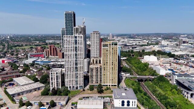 New build to rent apartment towers with coloured cladding stand together above workshops and warehouses in west London under a clear blue sky
