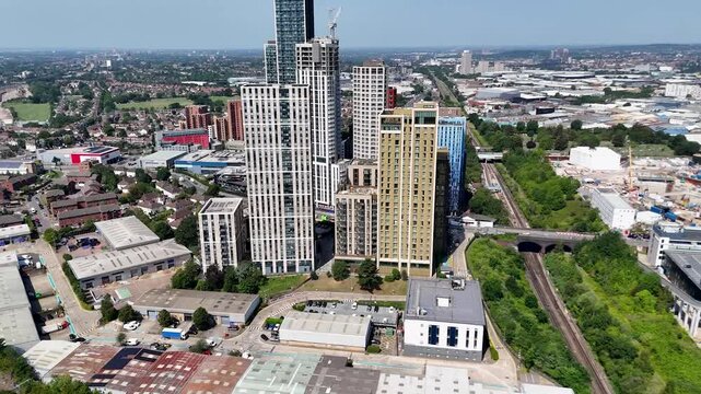 Cluster of new residential towers in white, blue and yellow cladding rises above low industrial units and a railway line in a regenerating west London district