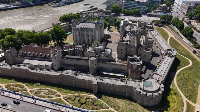 The Tower of London seen from above with its concentric curtain walls, the White Tower keep and moat gardens beside the riverside road