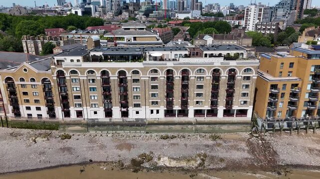 Converted riverside warehouse apartments with tall arched windows stand above the foreshore, beside modern brick blocks