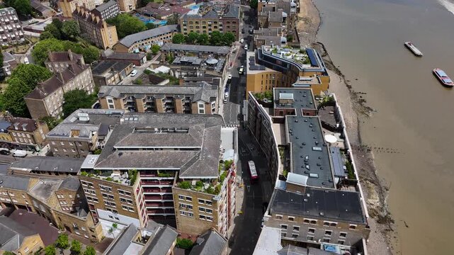 Aerial view of riverside streets and converted warehouse buildings beside the tidal foreshore, with a boat passing on the water