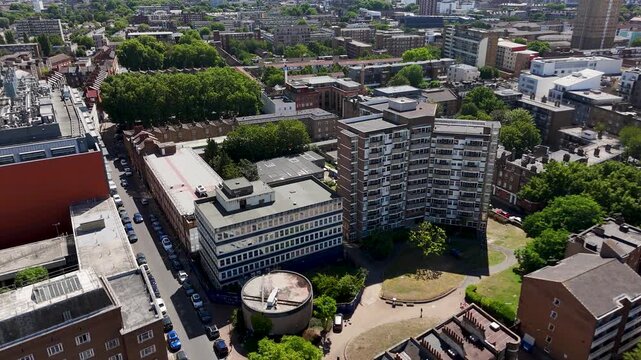 Postwar tower block and a low rise office building stand beside a small green and a car park in a dense inner city district
