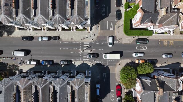 Top down view of a road junction with a zebra crossing, bus stop markings and cars waiting between rows of terraced roofs