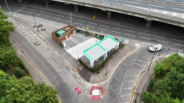Rapid electric vehicle charging station with green roofed canopies stands on a slip road beneath an urban motorway