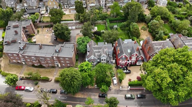 Large Edwardian houses and a red brick mansion block stand among mature trees on a quiet suburban street