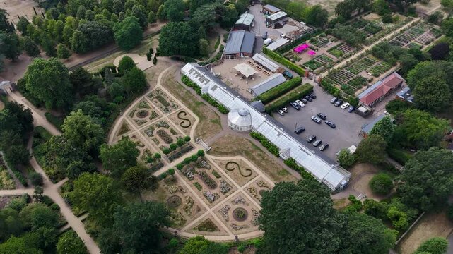 Long white conservatory and geometric formal gardens of a historic estate, with clipped hedges and scorched lawns after weeks without rain