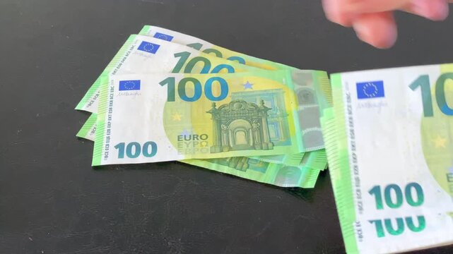 Close up of person counting stack of hundred euro banknotes on black background.