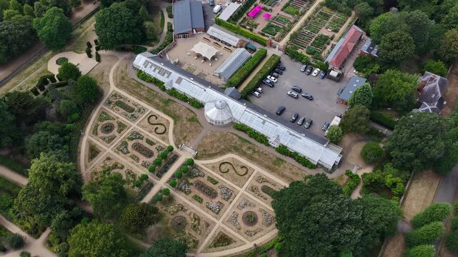 Ornate conservatory and formal parterre garden of a historic estate seen from above, with gravel paths and drought browned grass