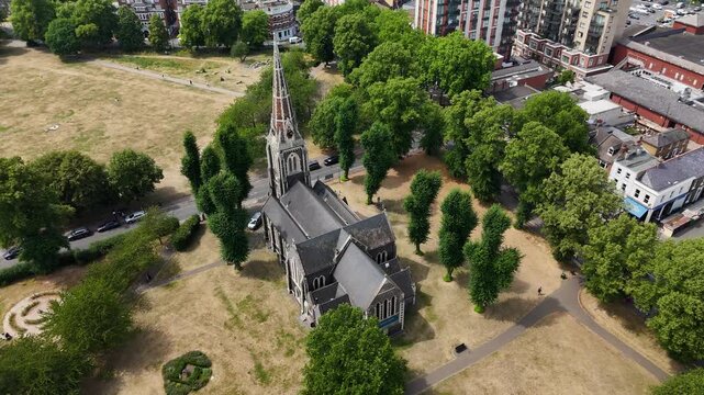 Gothic church and its churchyard trees stand on a scorched common, with a shopping parade along the road beyond