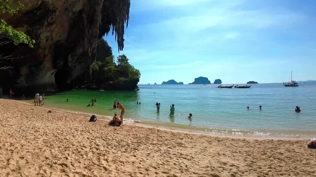 Stunning pan shot captures tourists enjoying the sun and clear waters of railay beach.