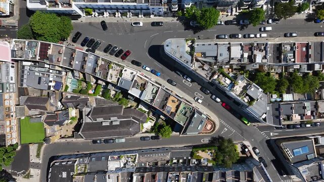 Top down view of a curving street of terraced roofs, chimney stacks and small rear gardens in a dense residential district