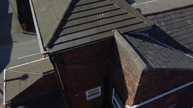 Aerial view of brick house roof showing grey tiles and chimney stack in residential area.