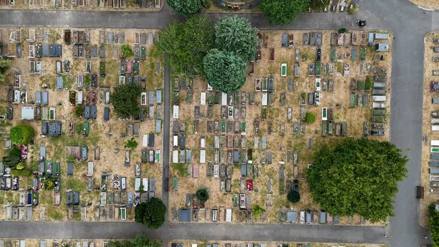 Top down view of dense rows of graves and family memorials in a cemetery, divided by paths and scattered trees