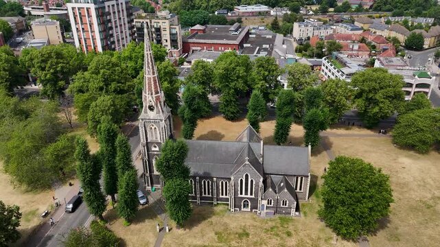 Stone gothic church with a slender spire seen from above on a drought browned common, framed by mature trees