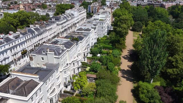 Sweeping terrace of grand white stucco houses with ornate porches and balconies curves beside a large private communal garden