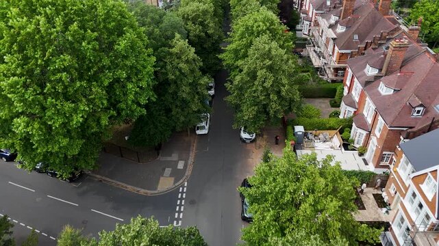Top down view of a quiet west London residential junction where mature trees shade the road between large houses