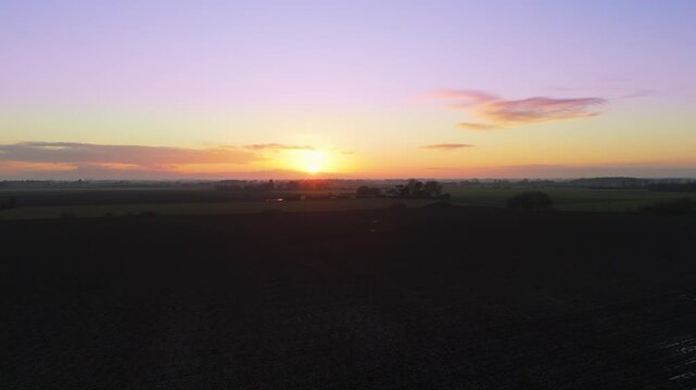 Sun dips low, painting sky in soft purple and gold. Fields stretch wide, darkened by twilight's slow approach. Silent landscape holds breath as day surrenders to night