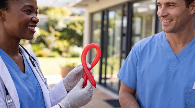A Black doctor holds a red ribbon balloon beside a Caucasian nurse near a hospital garden for National Red Ribbon Week hopeful images.