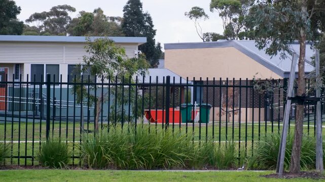 A modern public primary school buildings in campus behind black security fencing in Melbourne, Victoria, Australia. Public education infrastructure, student safety, and suburban community facilities.