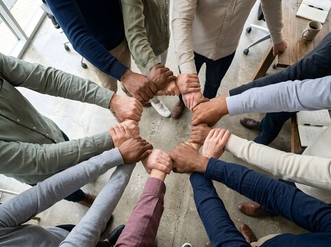 Diverse team members forming a tight circle of unity with hands clasped together in a modern office workspace setting