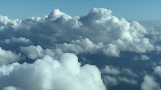Looking down on fluffy white clouds from airplane window during daytime flight.