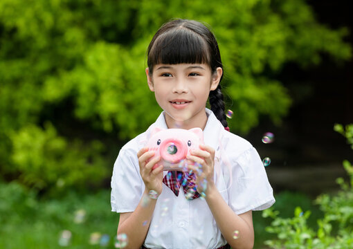 A young girl in a school uniform playing with bubbles outdoors