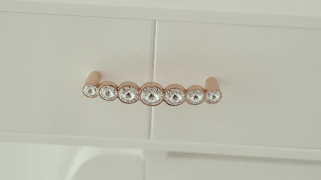 Close up of sparkling crystal and gold drawer handle on modern white furniture