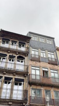 Vertical video from phone on traditional Portuguese residential buildings in downtown city of Porto. Facade with famous tiles called azulejos making colorful patterns on exterior walls. POV low angle