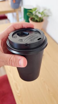 POV of man holding hot drink in black takeaway cup with coffee or tea inside office or studio. Enjoying coffee break in morning or afternoon after buying in store or local organic cafe. UGC style reel