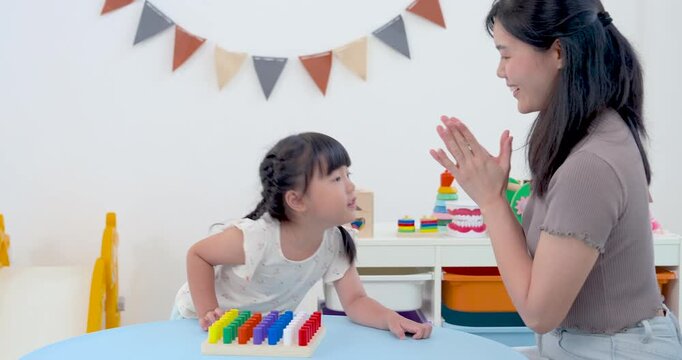 Asian single mother claps for preschool daughter after matching peg pieces on learning board, celebrating progress, confidence, and joyful parent child bonding during educational play at home.