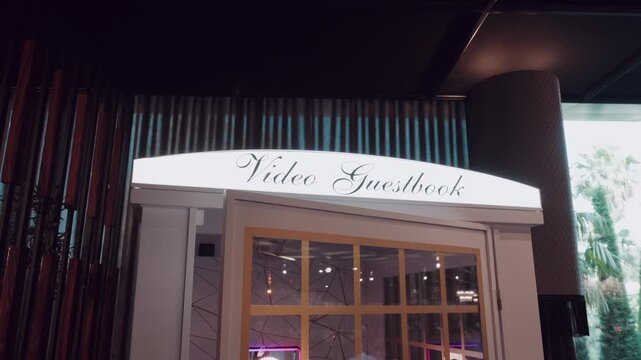 White Phone Box Style Video Guestbook Booth with Script Lettering inside an Event Venue