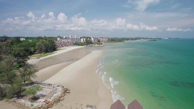 Aerial footage passes an abandoned seaside villa built above tropical waters, revealing vacant resort infrastructure, sandy beach and developed Malaysian coastline.
