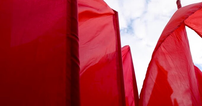 Large red cloth banners on vertical flagpoles, several red banners flutter outside against a white cloudy sky