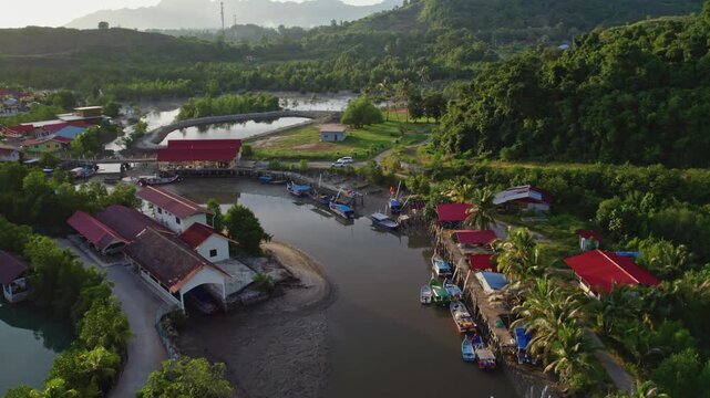 Cinematic drone flyover of a traditional fishing village nestled beside a winding tidal waterway, surrounded by mangroves and tropical hills in Langkawi, Malaysia.