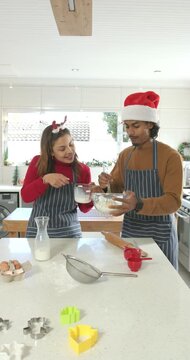 Vertical video: Diverse couple in aprons pouring milk into bowl, whisking batter in festive kitchen