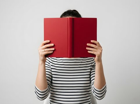 Focused Reader Immersed Behind a Bold Red Book Cover with Striped Sweater Clothing in Minimalist Lighting Composition