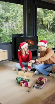 Vertical video: Upon unrolling ribbon, couple wrapping gifts for Christmas beside stove