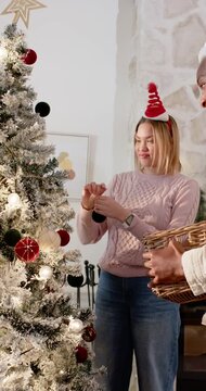 Vertical video: African American couple trimming tree home basket urging woman hanging ornament