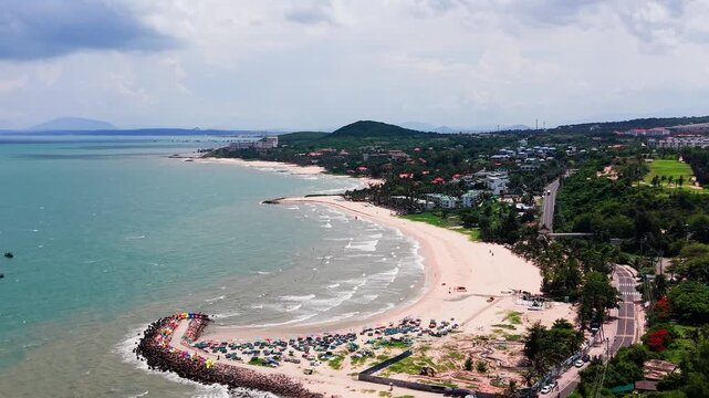 Visit Ong Dia Rock Beach in Phan Thiet, Vietnam. Observe the shoreline, waves, and distant hills. Enjoy the view of the beach on a sunny day with people relaxing and swimming.