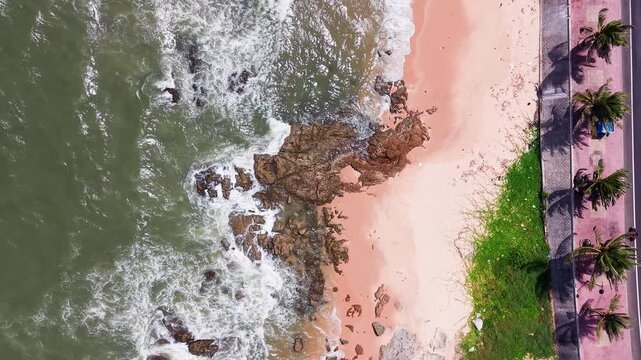 Visitors enjoy Ong Dia Rock Beach in Phan Thiet. The beach has soft sand and clear water. Waves crash on rocks as people walk along the shore in the bright sun.