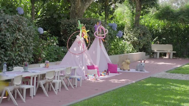 Pink play tents kids tables and ride on toys arranged in a garden for a childrens party