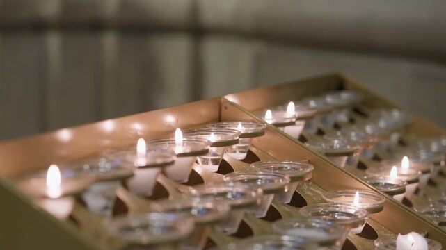 Small Votive Candles Burning In A Brass Rack Inside A Dim Church Interior