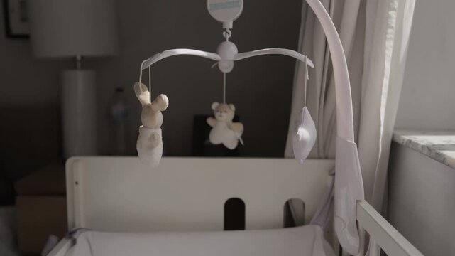 Plush bunny star and bear hanging from a cot mobile above an empty white baby crib