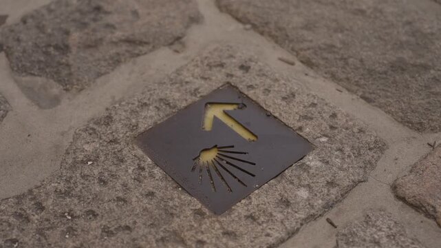 Metal Camino de Santiago marker with yellow arrow and scallop shell set in cobblestones