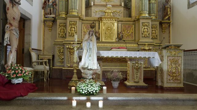 Nossa Senhora de Fatima statue with candles and flowers before a gilded altar and crucifix