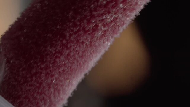 Macro close-up reveals red makeup brush bristles with soft fibers and textured surface, highlighting detailed cosmetic applicator texture under warm light