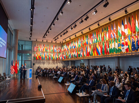 Global diplomatic summit featuring multiple international flags and delegates gathered in a large conference hall