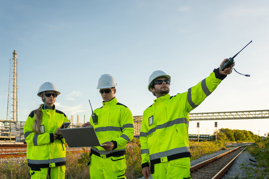 Engineers with laptop and walkie talkie working at oil refinery plant, petroleum plant team of engineers inspecting industrial facility site, energy industry professionals working together outdoors