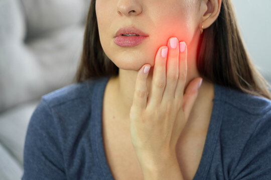 Young woman holding her cheek while suffering from painful jaw bruxism due to night stress
