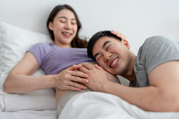 Fototapeta premium Asian husband and pregnant wife lying down together on bed in bedroom.